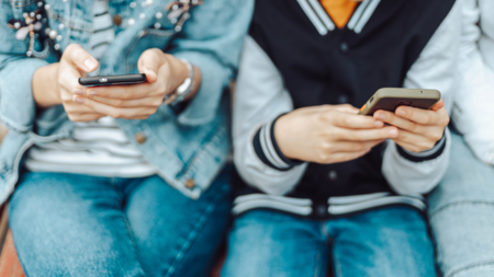 zwei Teenager sitzen nebeneinander und halten ihre Smartphones in der Hand.